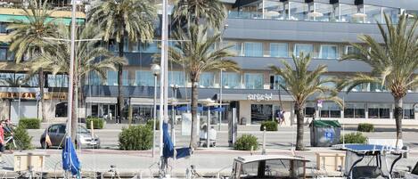 Un hotel de diseño moderno, con balcones y una vista despejada del puerto deportivo con barcos amarrados.