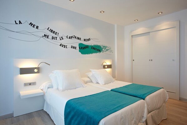 A modern bedroom with two beds, a teal bedspread, and a wall with motivational text. - Hotel Costa Azul (Palma de Mallorca)