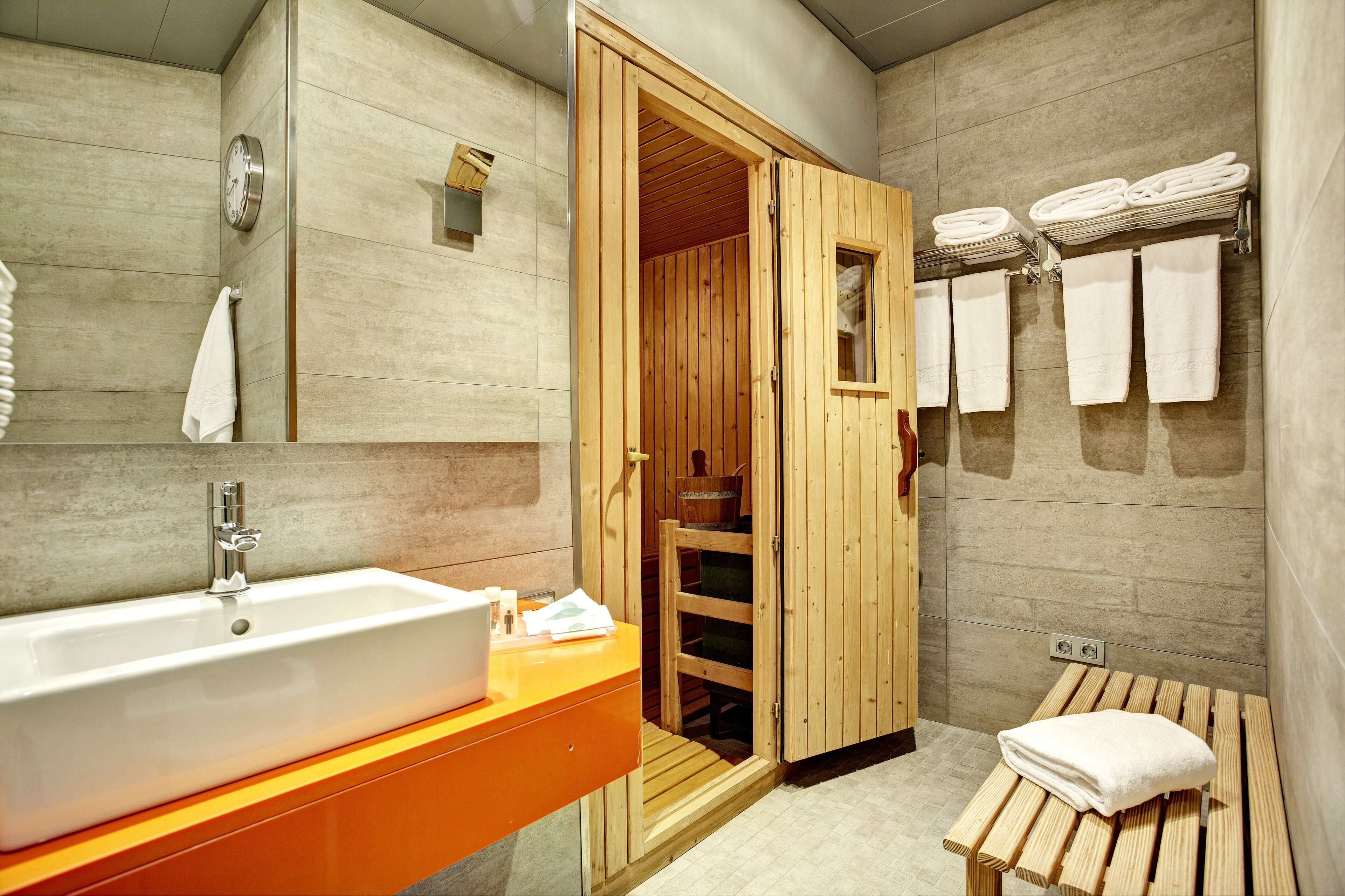 Un baño moderno con sauna de madera, un lavamanos grande y toallas ordenadas.