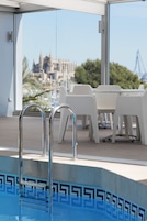 Zona de piscina con vistas a un edificio histórico, sillas blancas y una escalera metálica para la piscina.