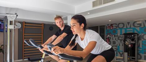 A gym with stationary bikes, a wall-mounted rack, and various exercise equipment.