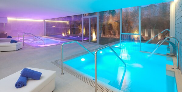 A modern indoor pool area with glass walls, a seating area with towels, and a spa-like ambiance. - Hotel JS Palma Stay - Adults Only (Palma de Mallorca)