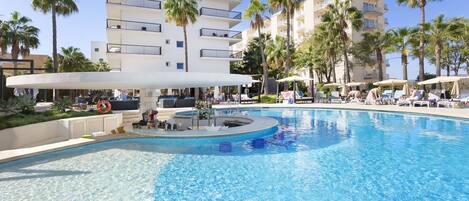 A swimming pool with lounge chairs and umbrellas, surrounded by palm trees and modern buildings.