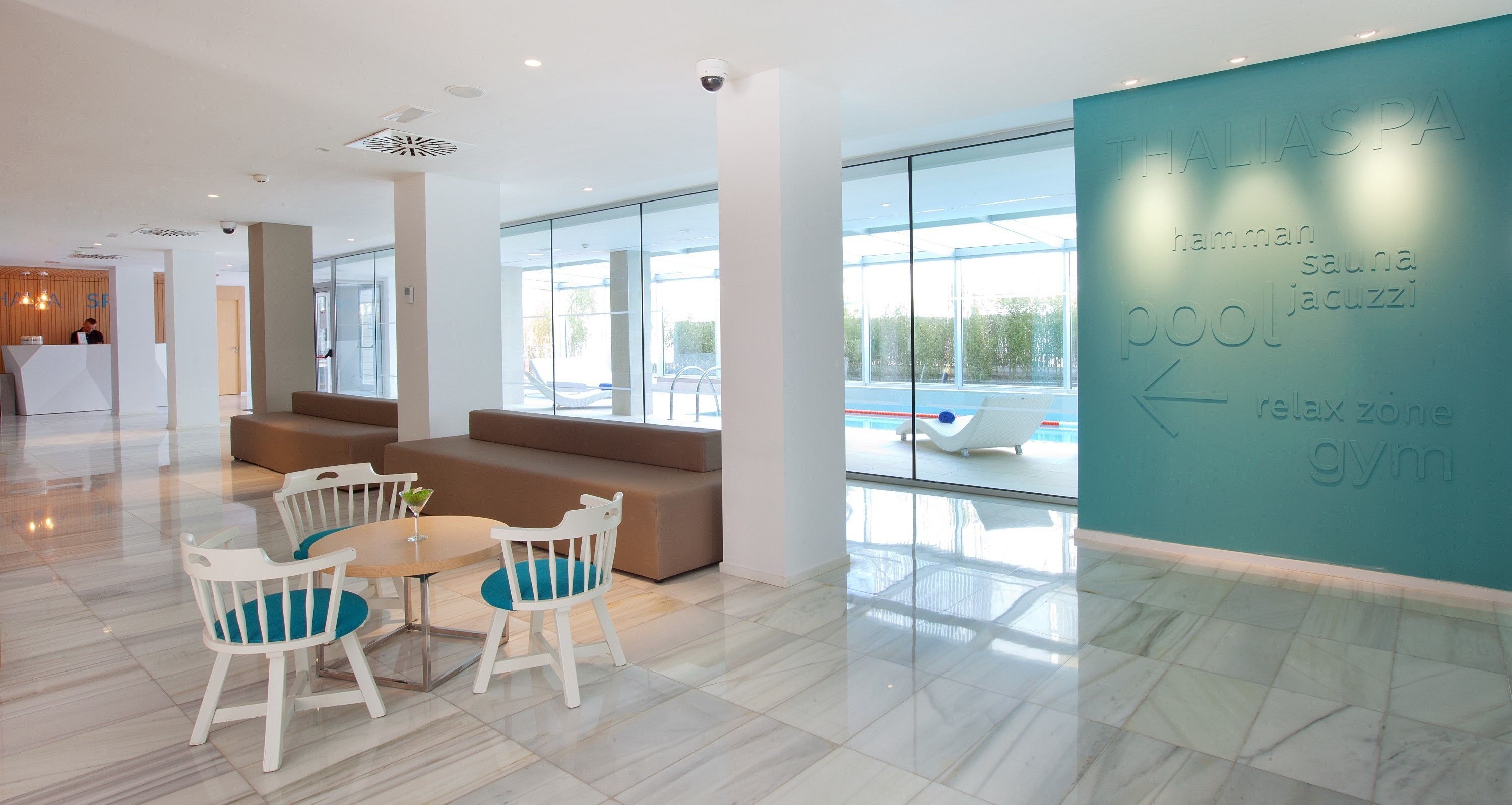 Um lobby moderno de hotel com balcão de recepção, área de estar e uma grande janela com vista para o exterior.
