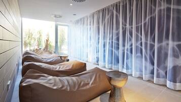 A spa room with three reclining chairs, a metallic lamp, and a large window with sheer curtains.