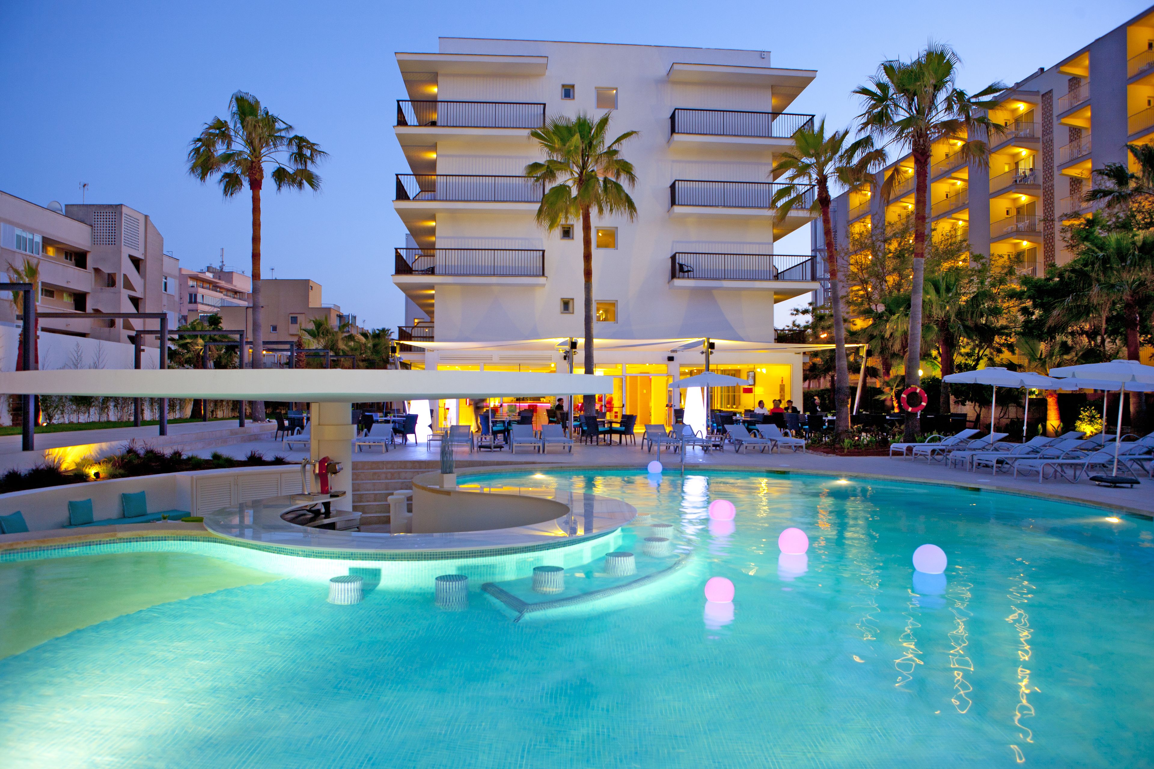 A hotel with a swimming pool, palm trees, and lounge chairs.