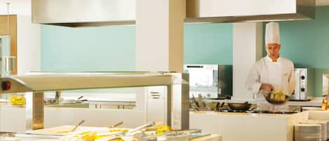 Une cuisine moderne équipée d’appareils électroménagers en acier inoxydable, un chef cuisinier en train de préparer des plats et un service de restauration de type buffet.