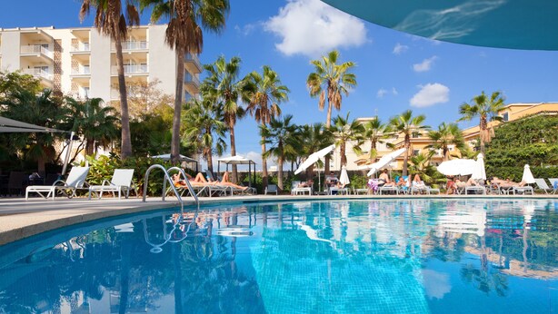 A swimming pool with lounge chairs and palm trees, surrounded by a building with balconies. - Hotel JS Palma Stay - Adults Only (Palma de Mallorca)