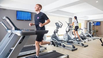 Une salle de sport équipée de tapis de course et de vélos d’appartement, avec un téléviseur accroché au mur et un plancher en bois.