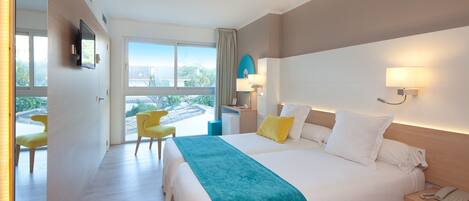 Habitación de hotel con una cama grande, un escritorio con teléfono, una silla, un televisor montado en la pared y una ventana con vistas a zonas verdes.