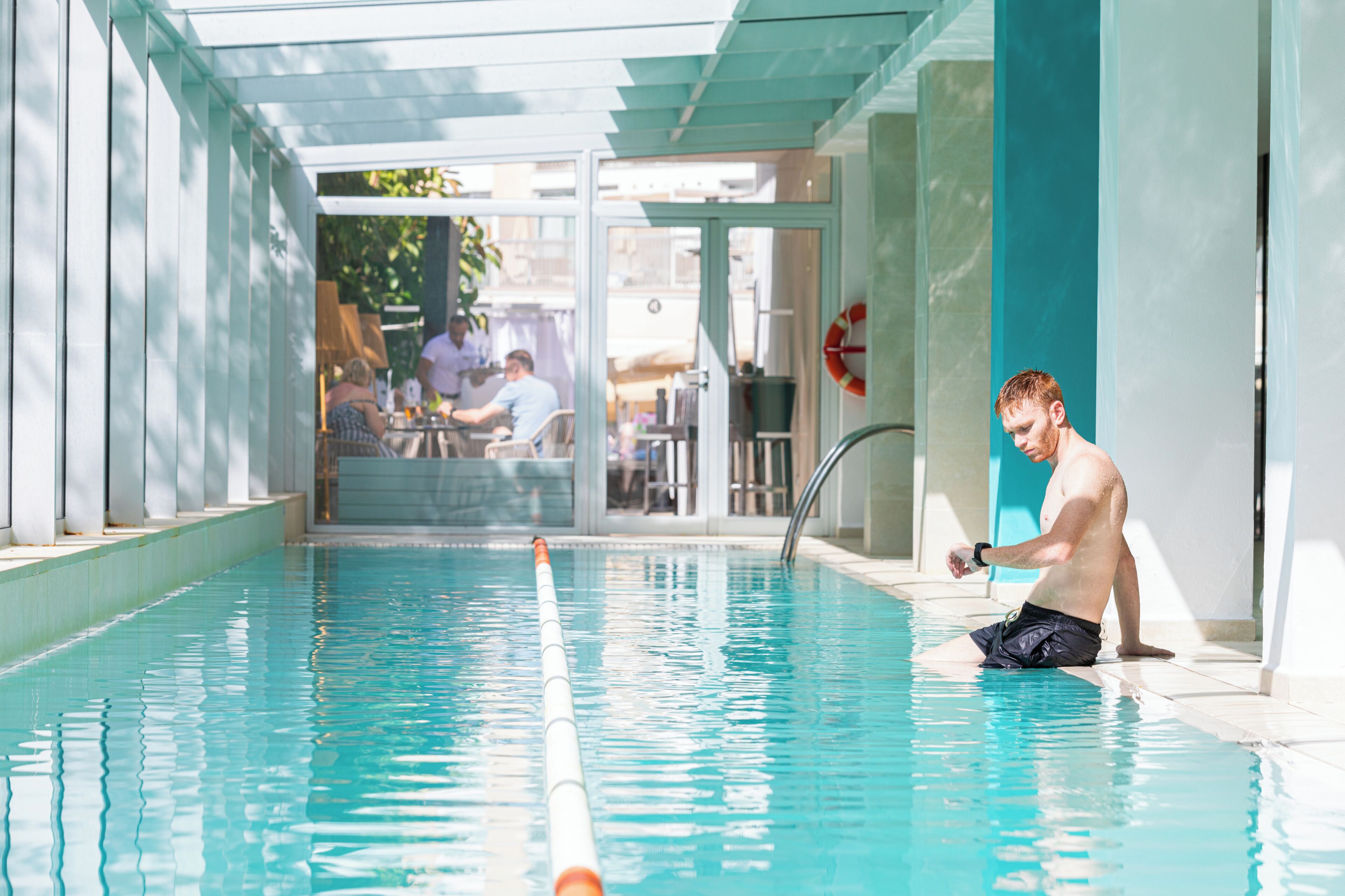Una piscina con trampolín, un flotador salvavidas y una puerta de cristal que da a un espacio al aire libre.