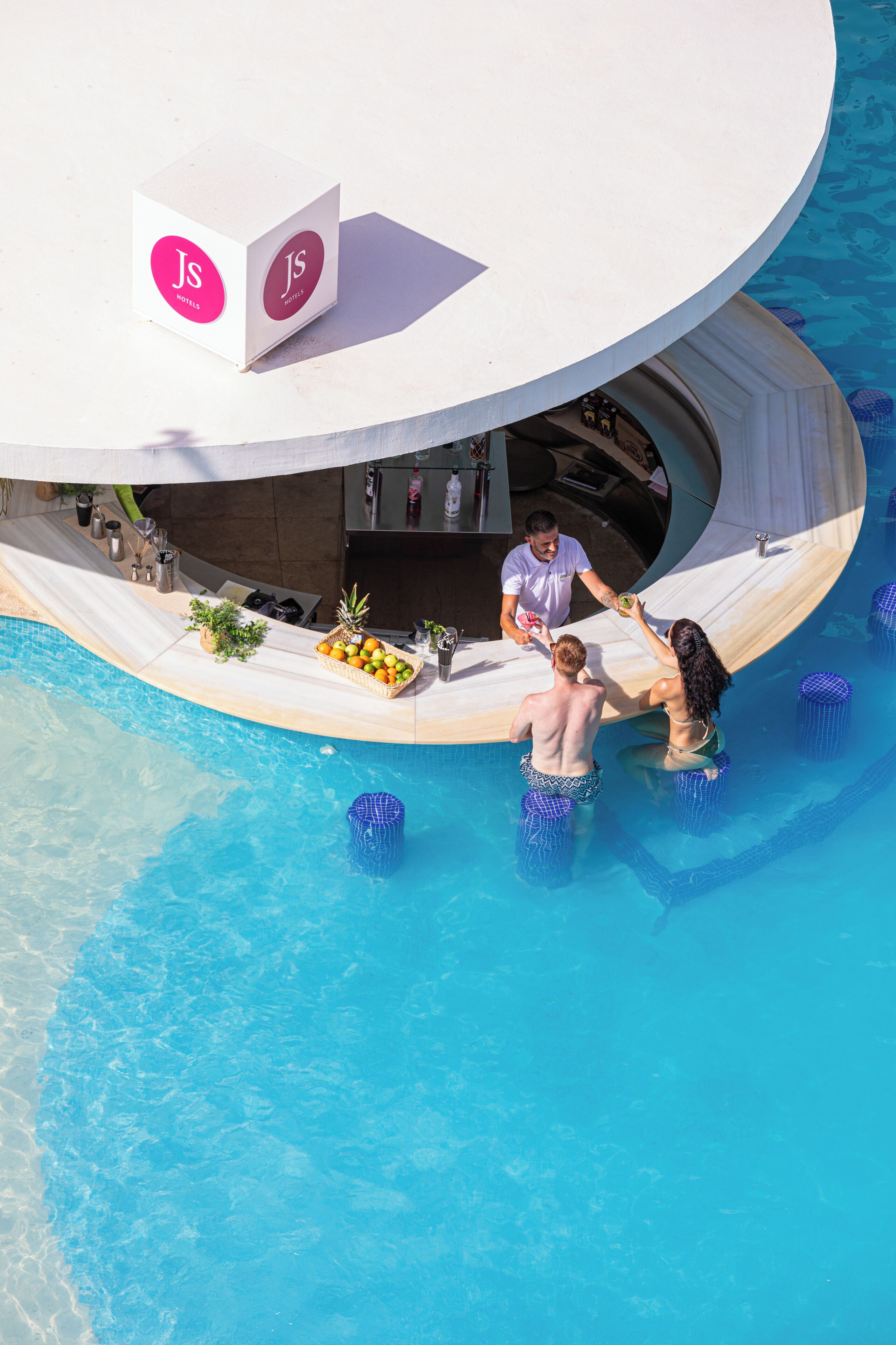 Un bar junto a la piscina con diseño circular, barra y zona de estar con planta y cesta de frutas.