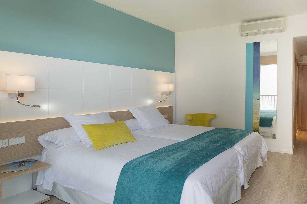 A hotel room with a bed, bedside tables, a mirror, and a desk with a lamp.