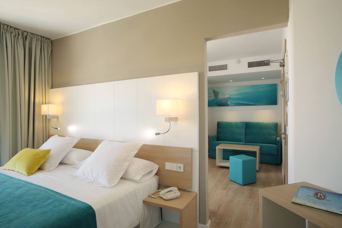 A hotel room with a bed, bedside lamps, a phone, a teal sofa, and a small table.