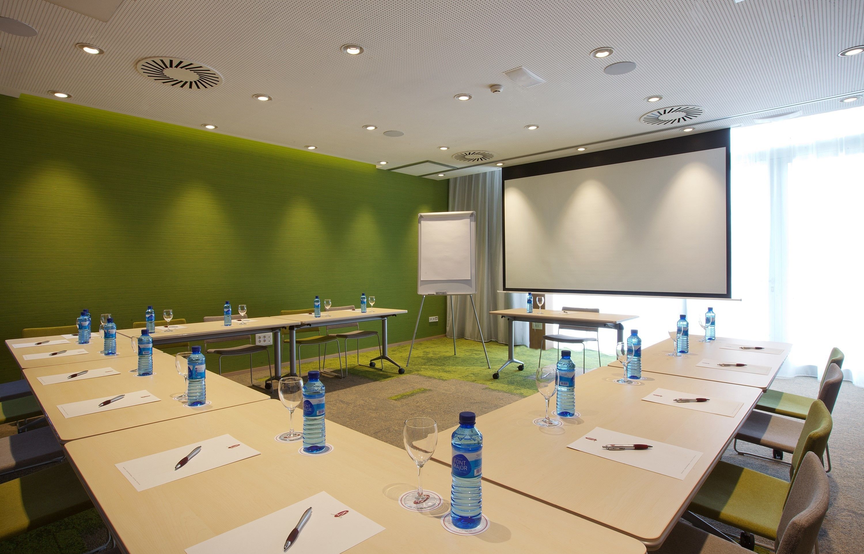 A conference room with long tables, water bottles, and a projector screen.