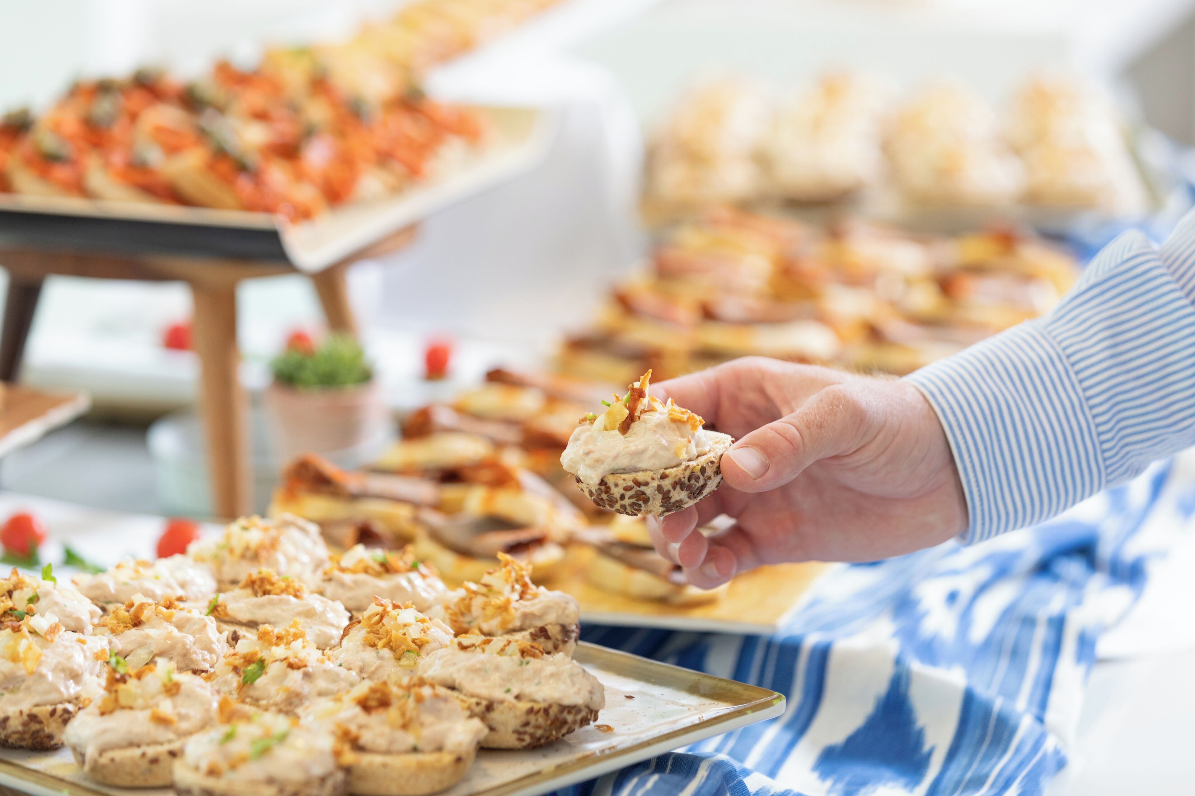 A hand holding a food item with a creamy topping, with other food items in the background.