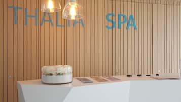 A reception desk with a wooden wall background, two hanging pendant lights, and a floral arrangement.