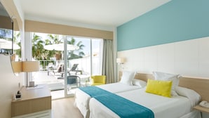A hotel room with a large bed, a desk with a lamp, a chair, and a view of the outdoor area with umbrellas and palm trees. - Hotel JS Palma Stay - Adults Only (Palma de Mallorca)