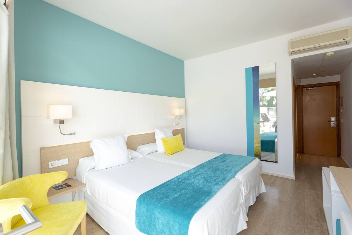 A hotel room with a bed, bedside tables, a chair, and a mirror.