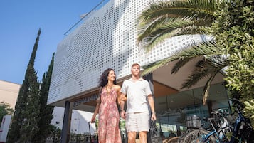 A modern building with a perforated facade, a palm tree, and bicycles parked outside.