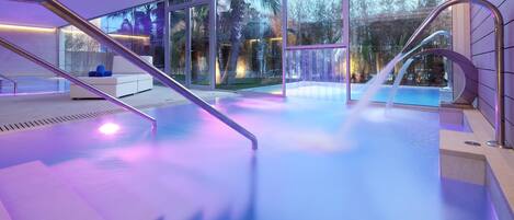 A modern indoor pool area with glass walls, a staircase, and a seating area.
