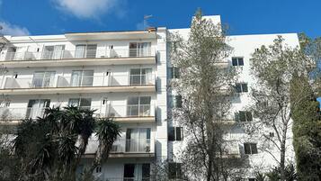 Un edificio residencial de varios pisos con balcones, paredes exteriores blancas y vegetación circundante.