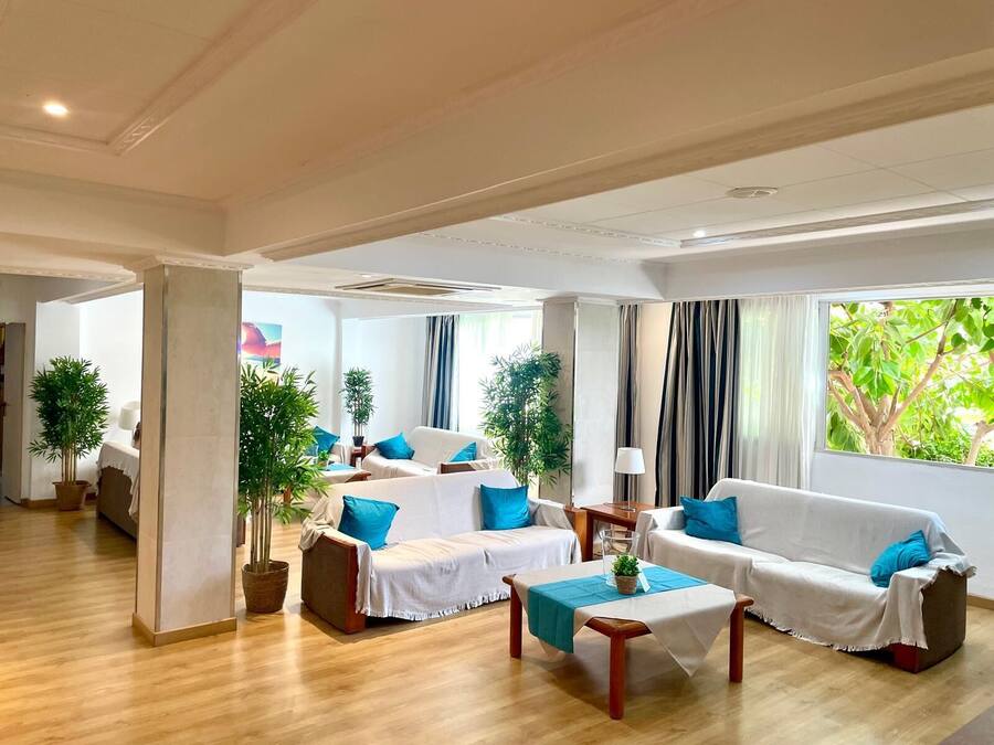 Un salón amplio con dos sofás blancos, una mesa de centro y varias plantas en macetas.