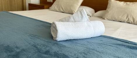 A neatly made bed with a blue bedspread, white pillows, and a folded white towel.