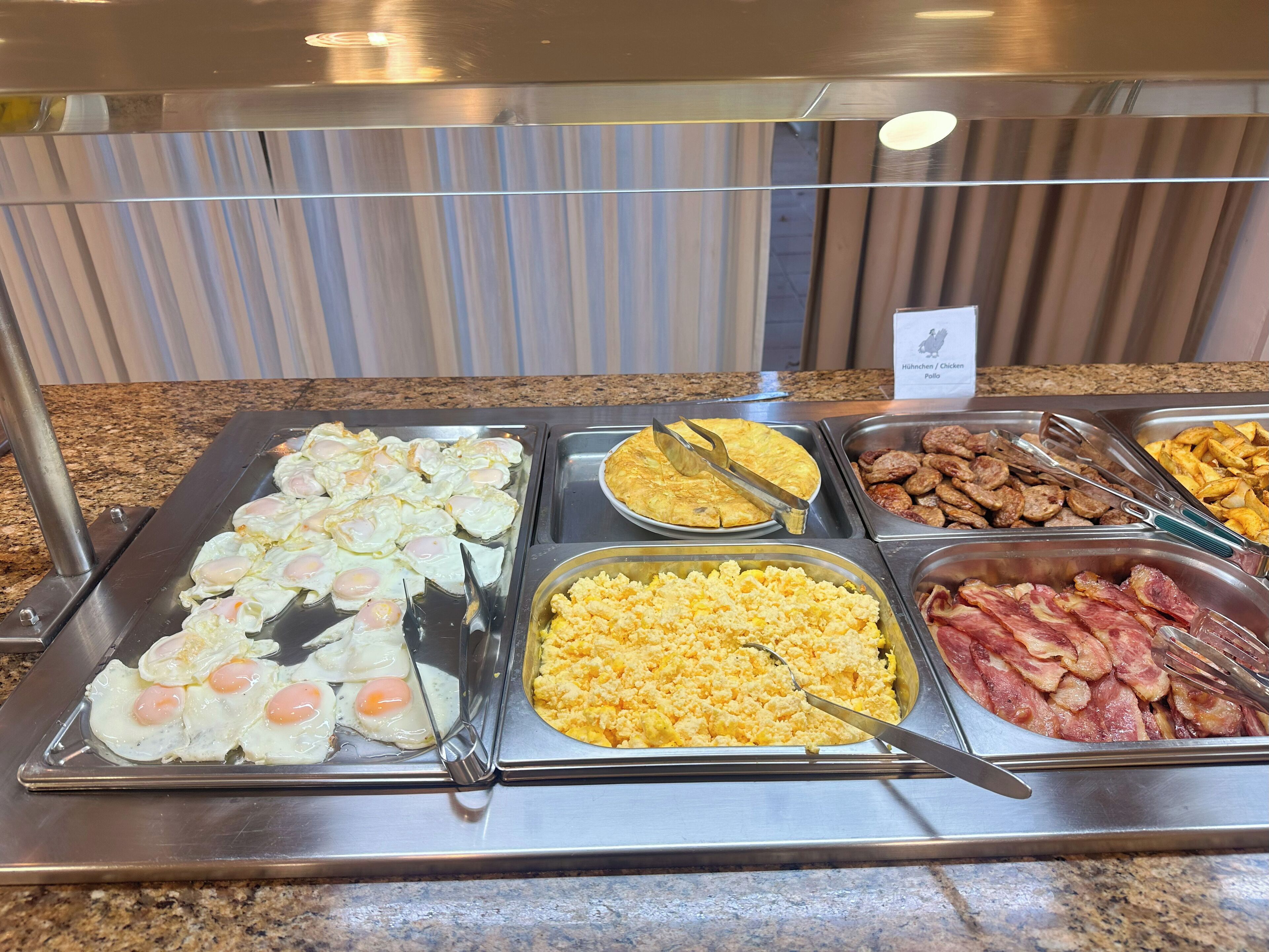 A buffet with various breakfast options including eggs, sausages, and bacon.