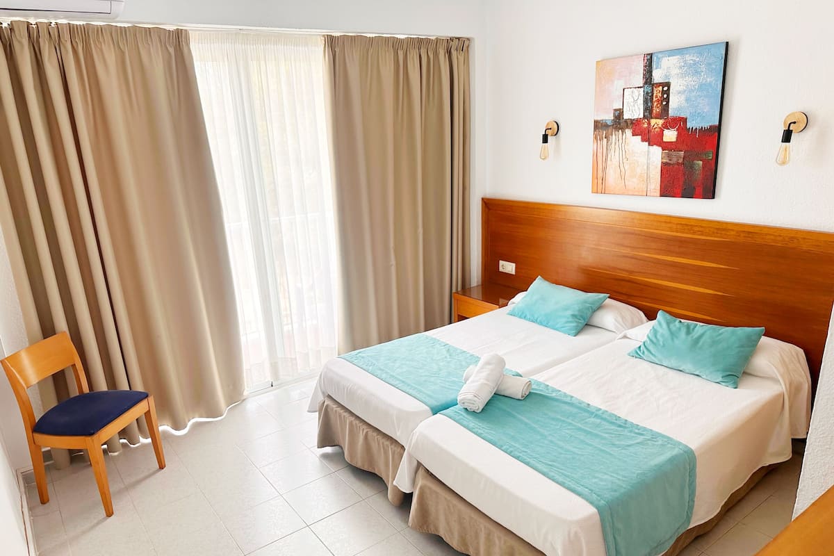 A hotel room with two beds, a wooden nightstand, a chair, and a painting on the wall.