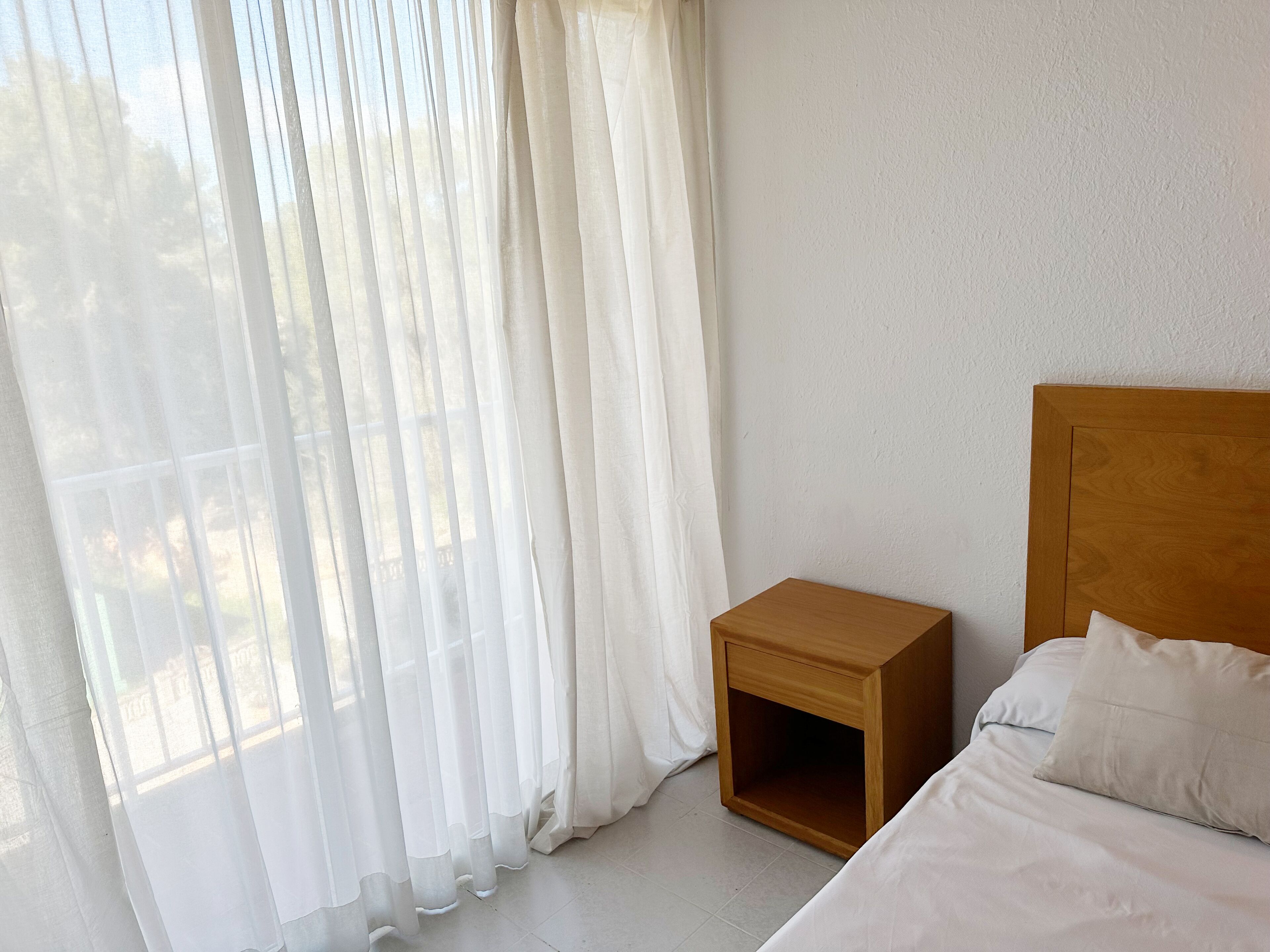 A bedroom with a wooden headboard, a wooden nightstand, and a bed with white bedding.