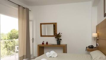 A hotel room with a bed, a bedside table with a lamp, a mirror, and a potted plant.