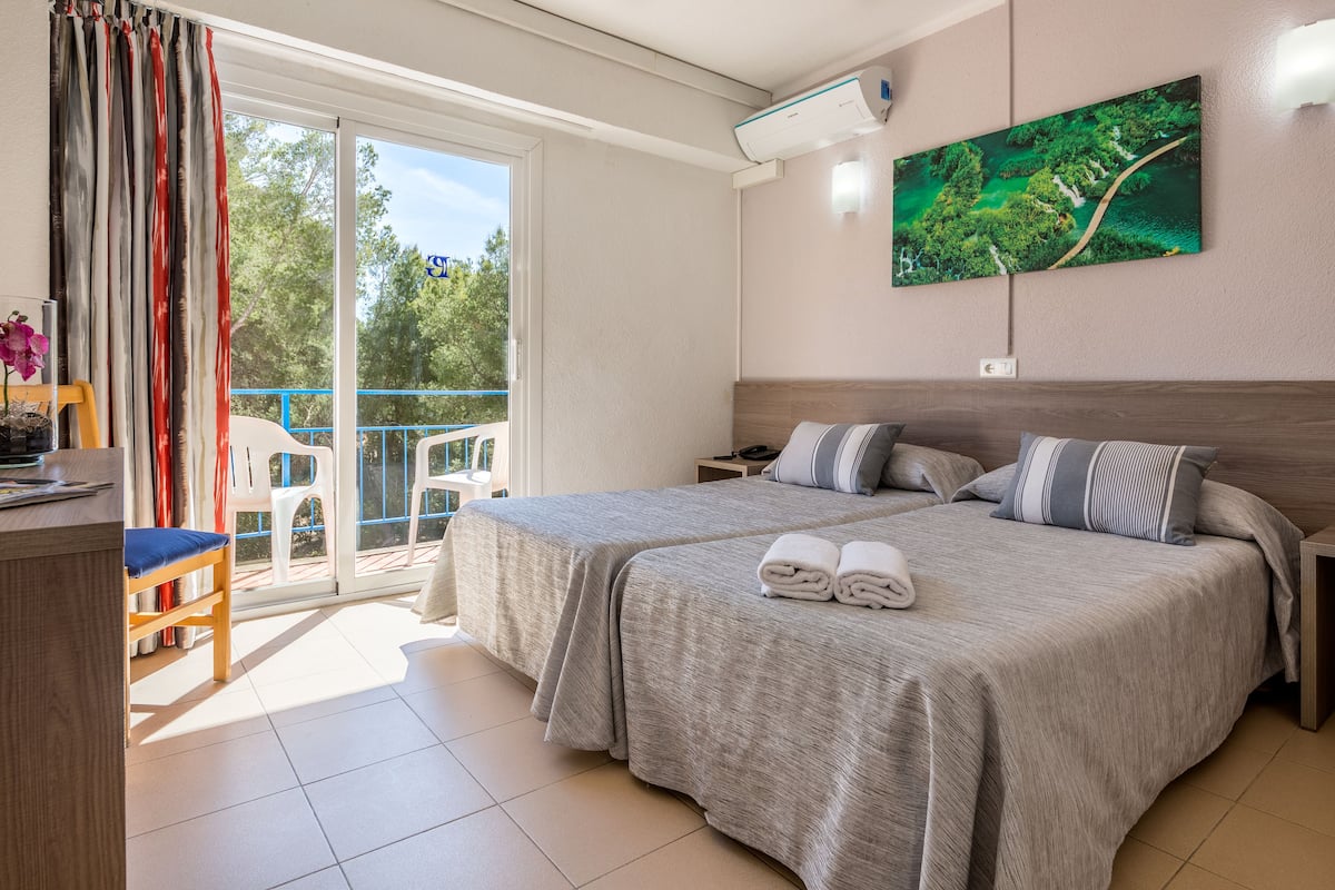 Ein Hotelzimmer mit zwei Betten, einem Balkon, einem Gemälde und einem Schreibtisch mit Stuhl.