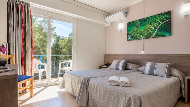 Una habitación de hotel con dos camas, un balcón, un cuadro y un escritorio con una silla.