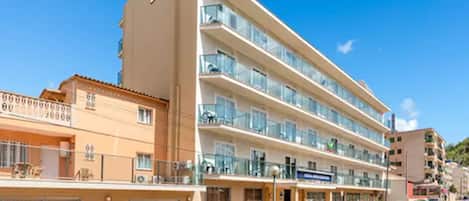 Un hotel de varios pisos con balcones, un estacionamiento y un cielo azul despejado.