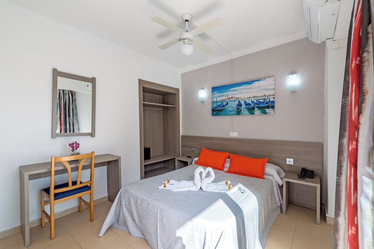 Ein Hotelzimmer mit Bett, Schreibtisch, Stuhl, Kleiderschrank und einem Bild an der Wand.