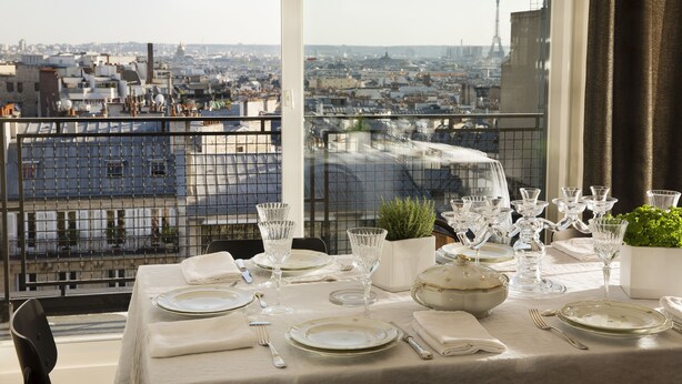A table set for dining with a city view, including the Eiffel Tower, on a balcony with a metal railing. - Hôtel Le Chat Noir (Paris)