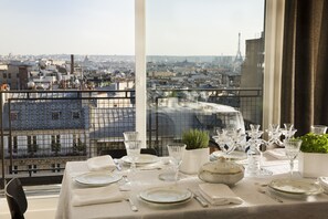 A table set for dining with a city view, including the Eiffel Tower, on a balcony with a metal railing. - Hôtel Le Chat Noir (Paris)