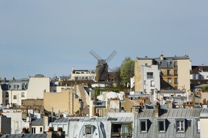 Un moulin à vent se dressant au milieu d’un quartier urbain densément peuplé, entouré de différents bâtiments et de toits.