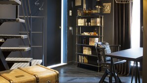 A modern interior with a dark color scheme, a spiral staircase, a vintage trunk, a dining area, and a bookshelf. - Hôtel Le Chat Noir (Paris)