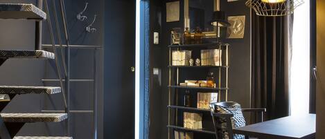 A modern interior with a dark color scheme, a spiral staircase, a vintage trunk, a dining area, and a bookshelf.
