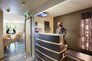 Et moderne receptionsområde med digital skærm, receptionsdisk og siddepladser med stole og borde.