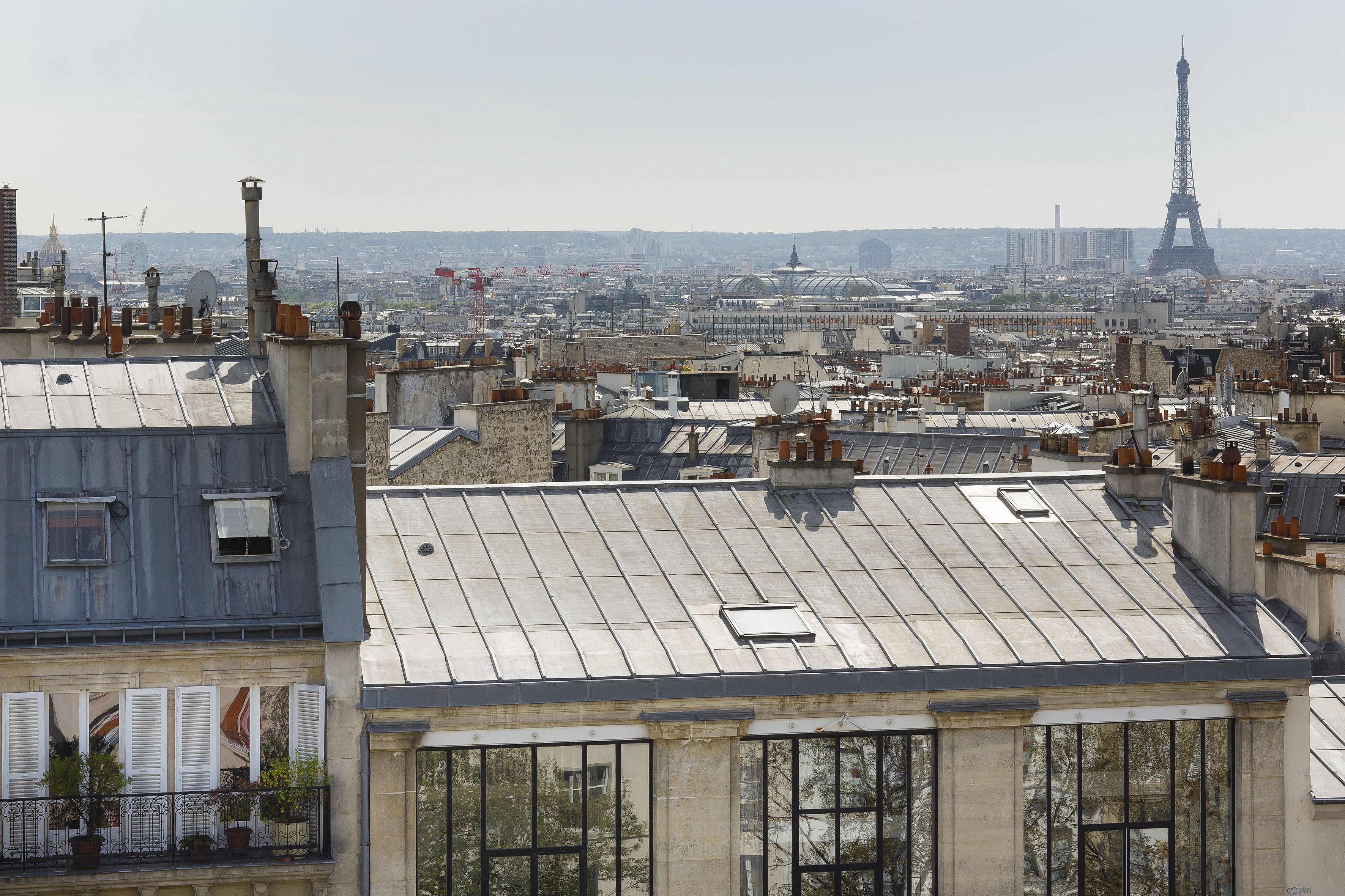 A cityscape with the Eiffel Tower in the distance, featuring rooftops and buildings with various architectural styles.