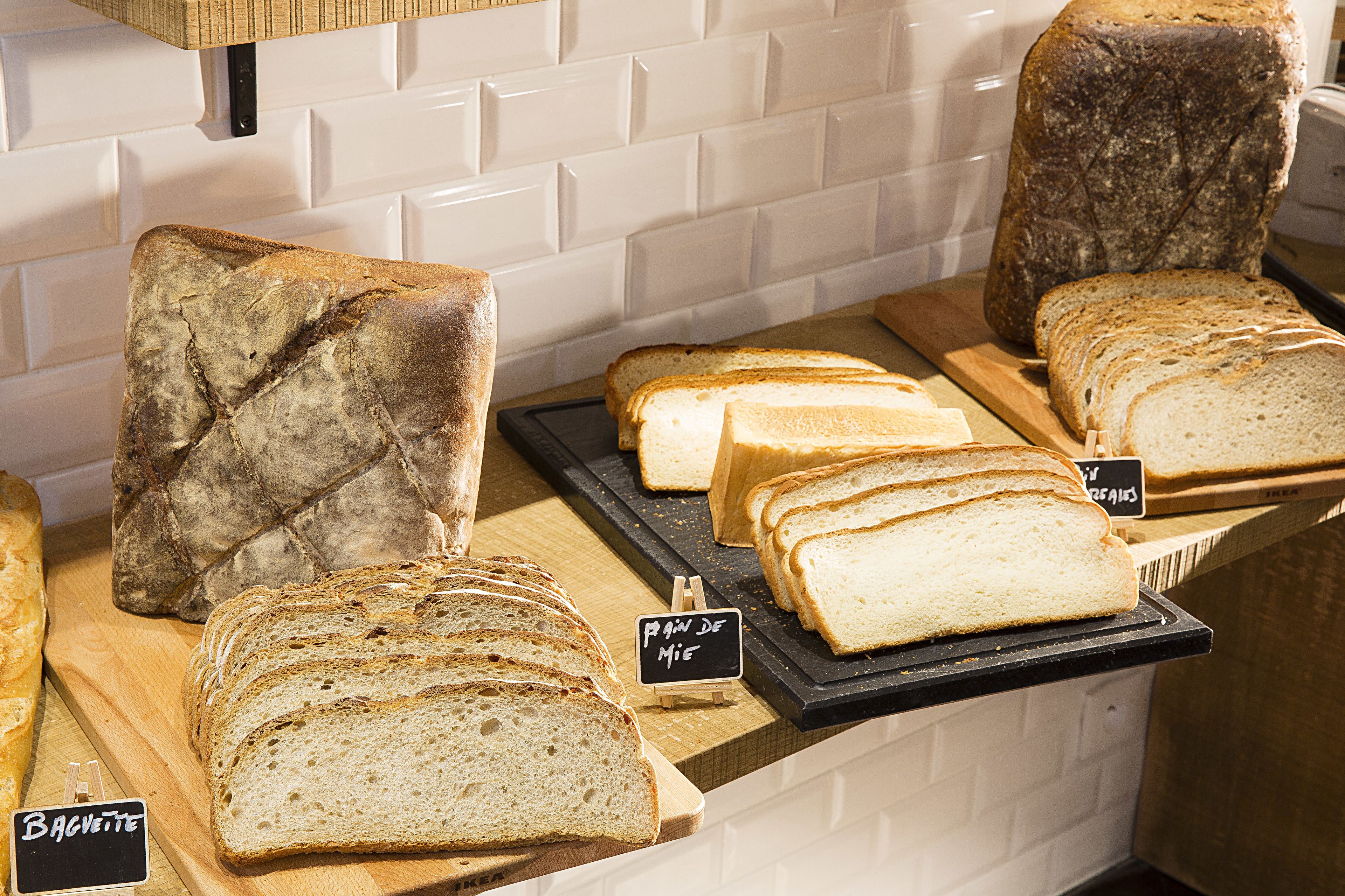 A bakery display with various types of bread, including baguettes and sliced loaves, arranged on wooden boards and a black tray.