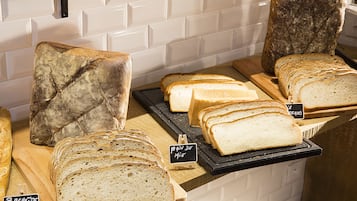 A bakery display with various types of bread, including baguettes and sliced loaves, arranged on wooden boards and a black tray.