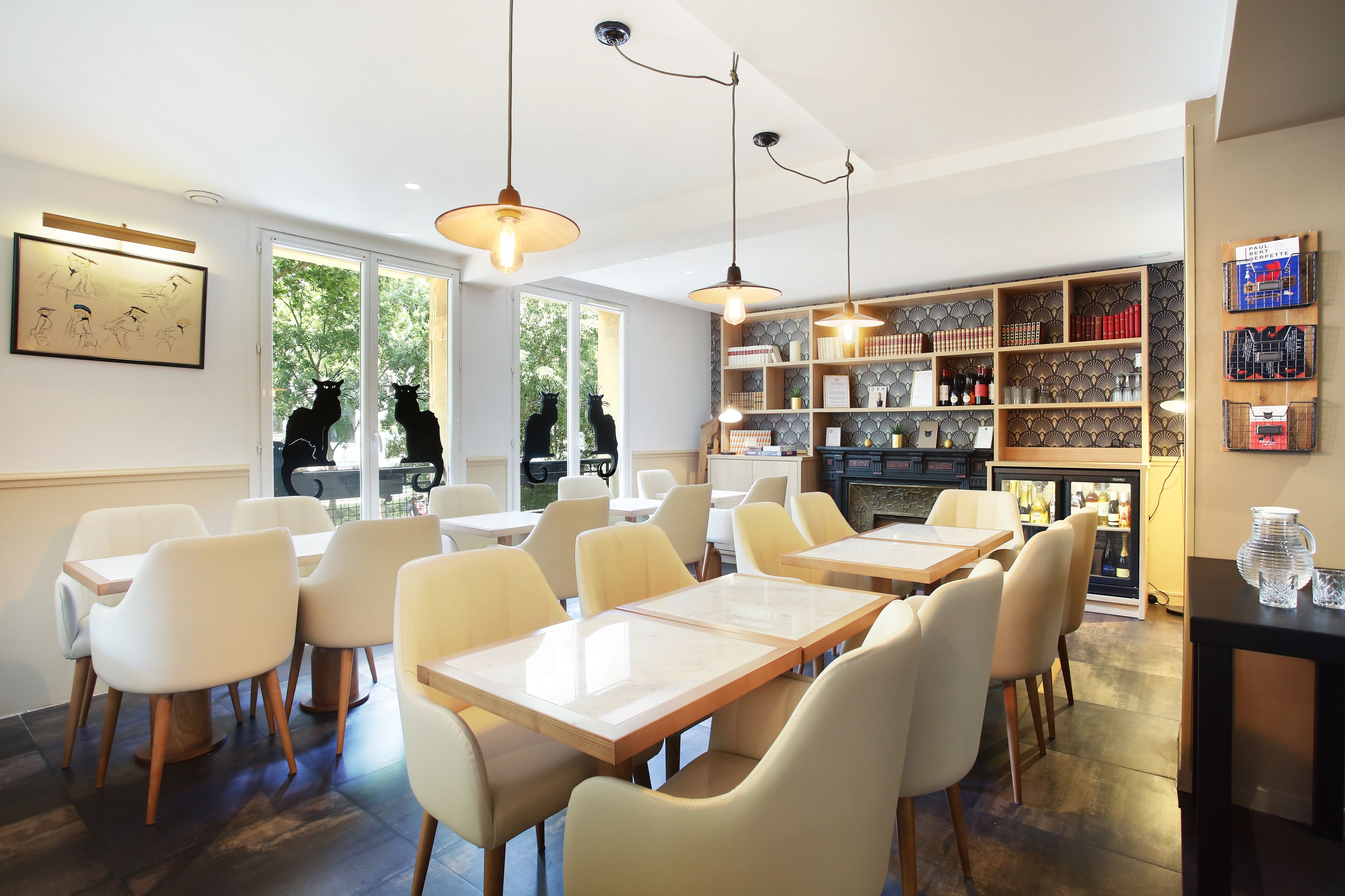 Un comedor moderno con sillas y mesas blancas, iluminación colgante y una estantería con diversos objetos.