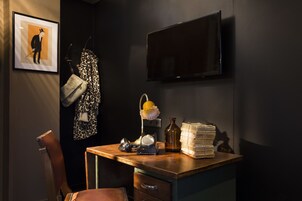 A room with a desk, a chair, a television mounted on the wall, and a framed picture.