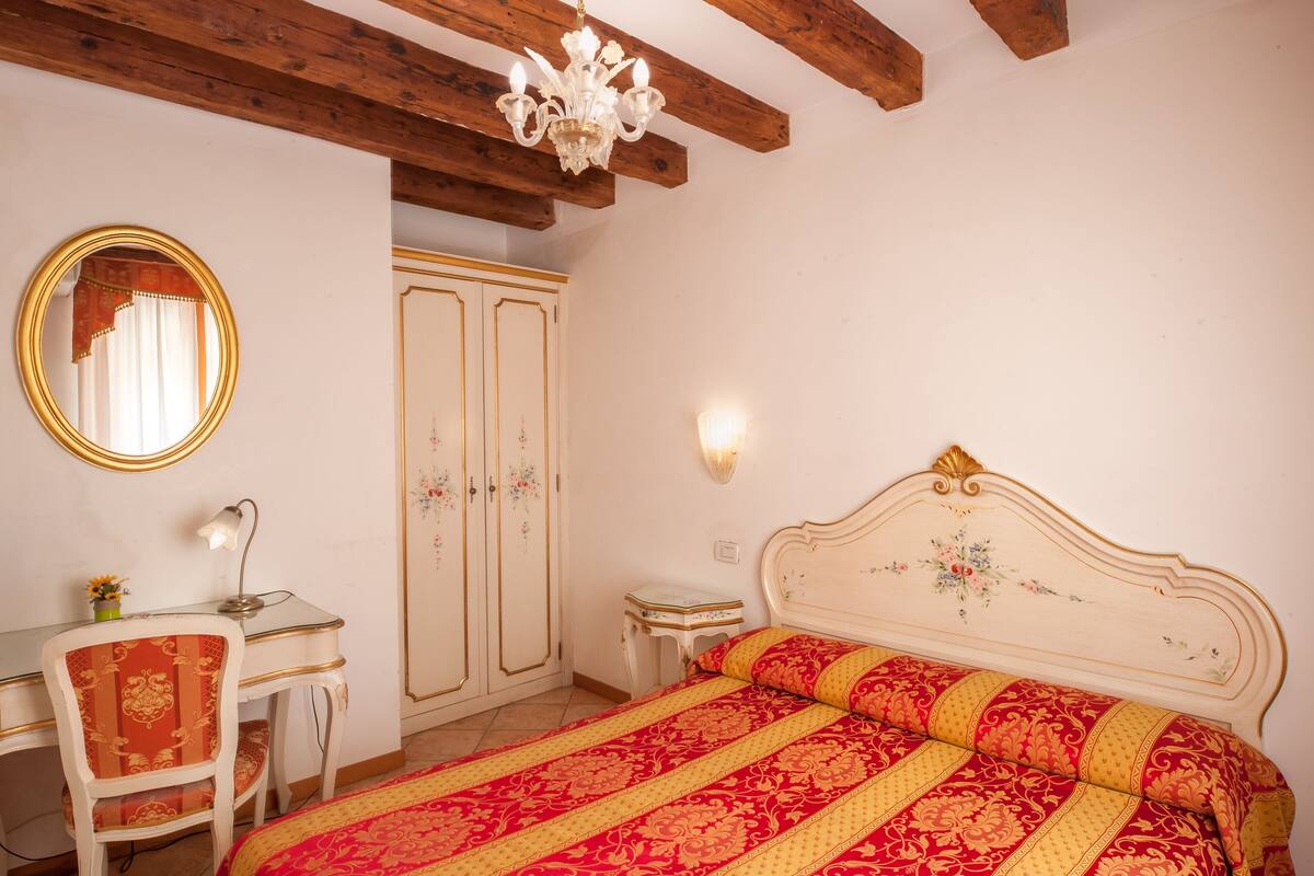 Une chambre à coucher comprenant un lit, un bureau, une chaise, une armoire et un lustre.