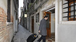 A narrow alley with a man pulling a suitcase, a building with a sign '381', and a door with a barred window.