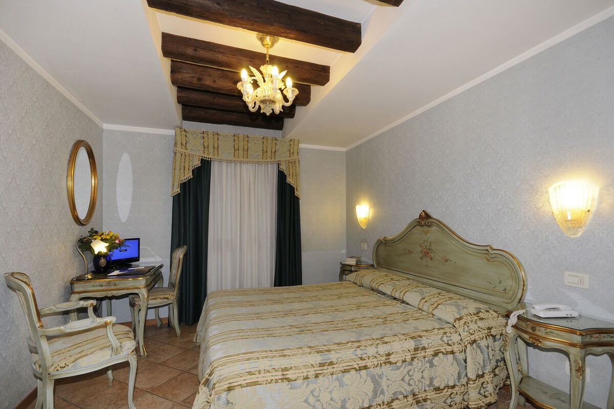Une chambre à coucher comprenant un lit, un bureau avec un ordinateur, une chaise, un lustre et un luminaire fixé au mur.